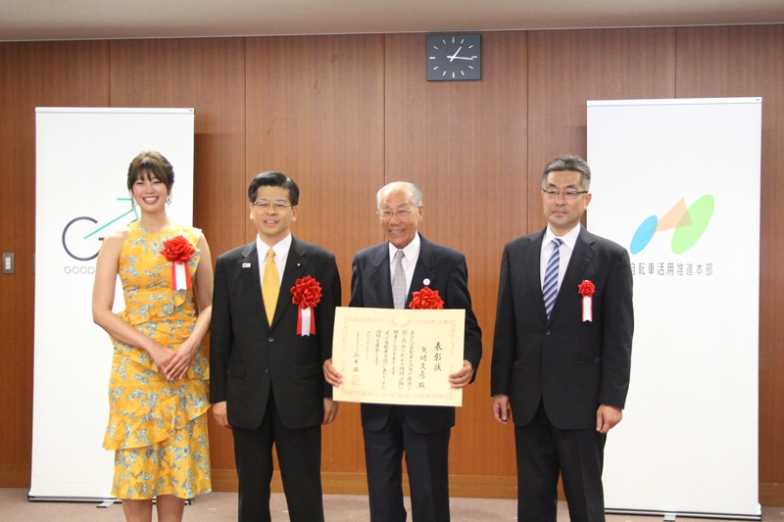 表彰状を持つ矢崎さん。98歳にして現役のサイクリストで、東京葛飾バイコロジー協会を設立し、自転車の安全利用や普及促進に尽力。年齢を聞いて石井大臣は驚いていた