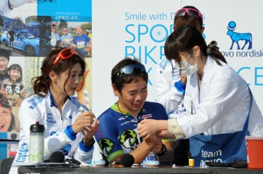 ゲストライダーとしてイベントに参加した益子直美さん(左)と山本雅道さん(中央)は、トークショーで夫婦揃って血糖測定を体験し、その簡単さをアピールしていた
